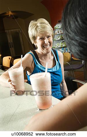 Stock Image - Mature Caucasian adult females sitting at table in health club cafeteria.. Fotosearch