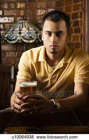 Portrait of serious young Hispanic man holding beer in pub. View Large Photo Image Stock Photo - Portrait of serious young Hispanic man holding beer in pub.. Fotosearch