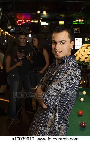 Stock Photo - Portrait of smiling young Hispanic man next to billiards table at pub.. Fotosearch