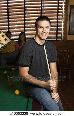 Portrait of young man leaning on billiards table holding pool stick. View Large Photo Image Stock Photo - Portrait of young man leaning on billiards table holding pool stick.. Fotosearch