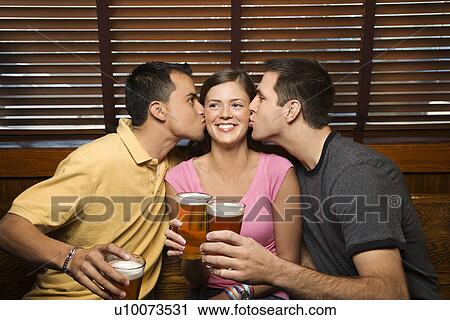 Stock Image - Two men kissing woman in the middle while holding their beers at pub.. Fotosearch