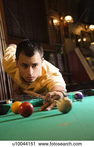 Young man concentrating while aiming at pool ball while playing billiards. View Large Photo Image Stock Image - Young man concentrating while aiming at pool ball while playing billiards.. Fotosearch