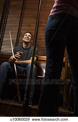 Stock Photo - Young man with billiards cue talking with woman standing before him.. Fotosearch