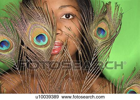 Stock Photo - African-American mid-adult woman looking through peacock feather.. Fotosearch