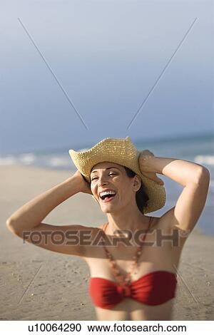 Caucasian mid-adult female laughing on beach in swimsuit holding hat on head. View Large Photo Image Stock Image - Caucasian mid-adult female laughing on beach in swimsuit holding hat on head.. Fotosearch
