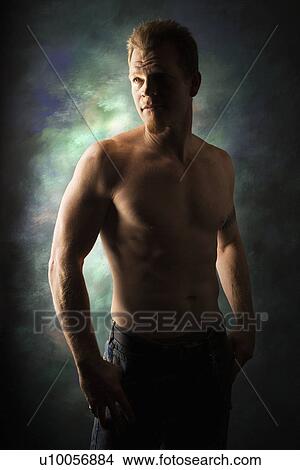Picture - Dramatically lit portrait of shirtless young adult Caucasian man on studio background.. Fotosearch