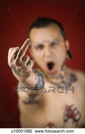 Stock Image - Caucasian mid-adult man with tattoos and piercings holding up middle finger.. Fotosearch