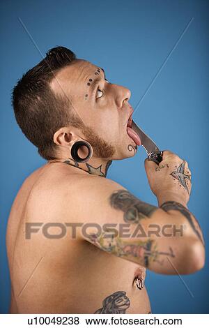 Stock Photo - Caucasian mid-adult man with tattoos and piercings holding knife to tongue.. Fotosearch