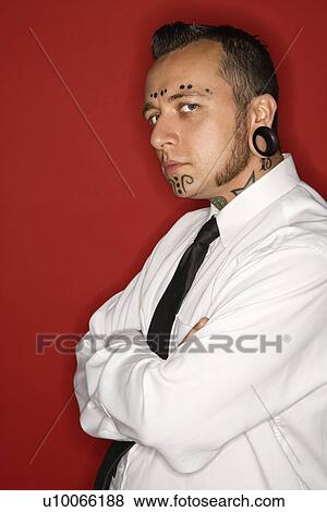Stock Photo - Caucasian mid-adult man with tattoos and piercings wearing necktie looking at viewer.. Fotosearch