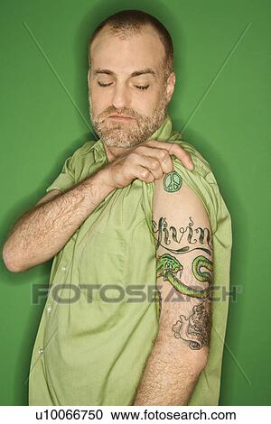 Portrait of Caucasian man pulling up sleeve to show tattoo standing against green background. View Large Photo Image Stock Image - Portrait of Caucasian man pulling up sleeve to show tattoo standing against green background.. Fotosearch