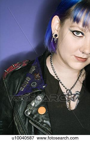 Stock Photo - Portrait of Caucasian woman with blue hair and black leather jacket against blue background.. Fotosearch