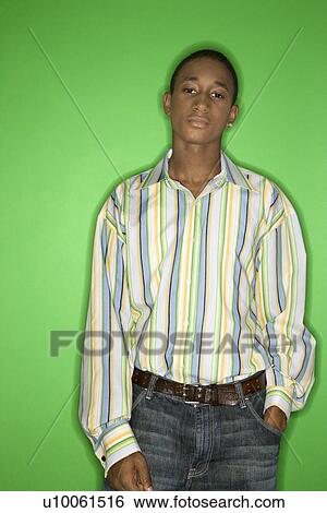 Stock Photograph - Portrait of African-American teen boy with one hand in pocket standing against green background.. Fotosearch