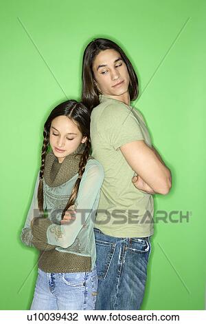 Stock Image - Portrait of Asian-American girl and teen boy standing back to back as boy looks down at girl over his shoulder.. Fotosearch