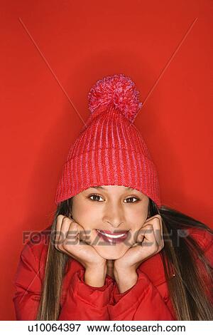 Portrait of Asian-American teen girl wearing winter hat resting head on hands against red background. View Large Photo Image Stock Photo - Portrait of Asian-American teen girl wearing winter hat resting head on hands against red background.. Fotosearch