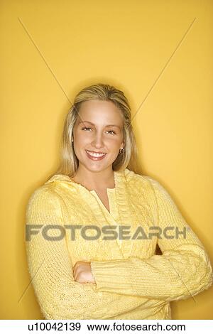 Stock Photo - Portrait of blond Caucasian teen girl smiling with crossed arms against yellow background.. Fotosearch