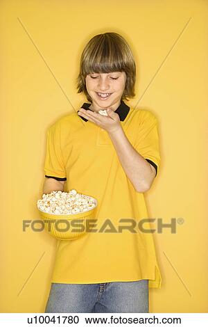 Portrait of Caucasian boy smiling holding bowl of popcorn in one hand and bringing some popcorn to mouth standing against yellow background. View Large Photo Image Stock Image - Portrait of Caucasian boy smiling holding bowl of popcorn in one hand and bringing some popcorn to mouth standing against yellow background.. Fotosearch