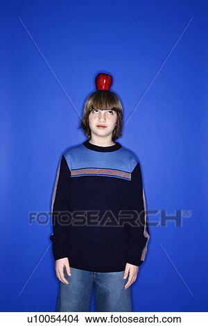 Portrait of Caucasian boy with an apple on his head standing against blue background. View Large Photo Image Picture - Portrait of Caucasian boy with an apple on his head standing against blue background.. Fotosearch