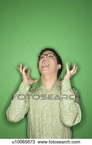 Stock Image - Portrait of Caucasian teen boy screaming with hands beside ears in front of green background.. Fotosearch