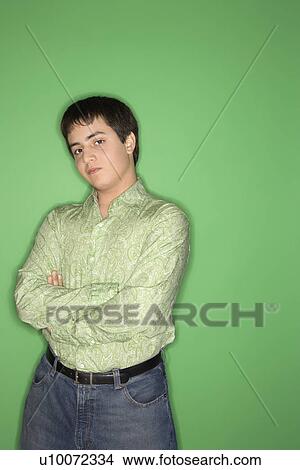 Picture - Portrait of Caucasian teen boy with crossed arms standing against green background.. Fotosearch