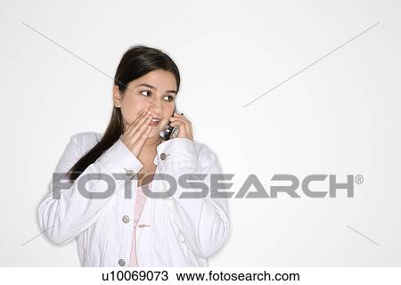 Stock Image - Portrait of Caucasian teen girl whispering into cellphone standing against white background.. Fotosearch