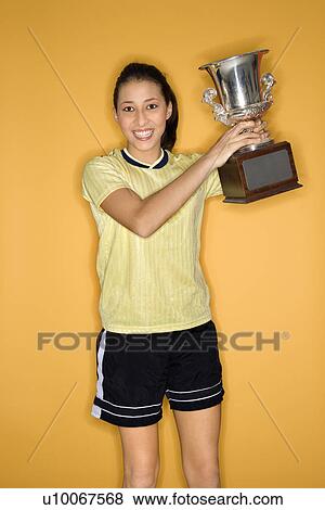 Portrait of Multi-racial teen girl in soccer uniform holding trophy and smiling standing against yellow background. View Large Photo Image Stock Photo - Portrait of Multi-racial teen girl in soccer uniform holding trophy and smiling standing against yellow background.. Fotosearch