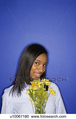 Stock Image - Portrait of smiling African-American teen girl with bouquet of flowers against blue background.. Fotosearch