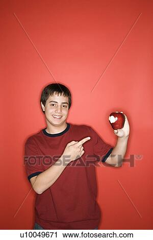 Portrait of smiling Caucasian teen boy pointing to partially eaten apple standing against red background. View Large Photo Image Stock Image - Portrait of smiling Caucasian teen boy pointing to partially eaten apple standing against red background.. Fotosearch