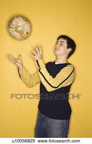 Portrait of smiling Caucasian teen boy tossing globe in air standing against yellow background. View Large Photo Image Stock Photo - Portrait of smiling Caucasian teen boy tossing globe in air standing against yellow background.. Fotosearch