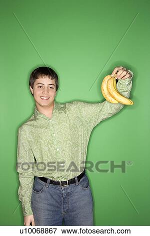 Stock Photo - Portrait of smiling Caucasian teen boy holding bananas in air standing against green background.. Fotosearch