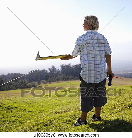 Stock Image - Pre-teen Caucasin male holding remote control and airplane standing on a grassy knoll.. Fotosearch