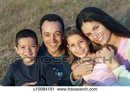 Stock Image - Family in park sitting in field. Fotosearch