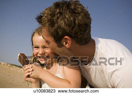 Stock Image - Father and daughter on beach with ice cream. Fotosearch