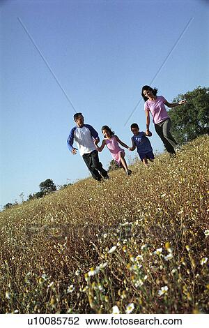 Stock Image - Family in park running in field. Fotosearch