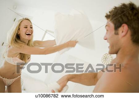 Stock Image - Couple in bedroom having pillow fight. Fotosearch