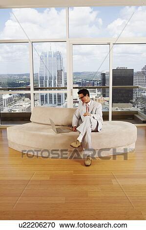 Businessman sitting on a couch and using a laptop View Large Photo Image Stock Image - Businessman sitting on a couch and using a laptop. Fotosearch