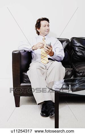 Stock Photo - Businessman sitting on a couch and holding a mobile phone. Fotosearch
