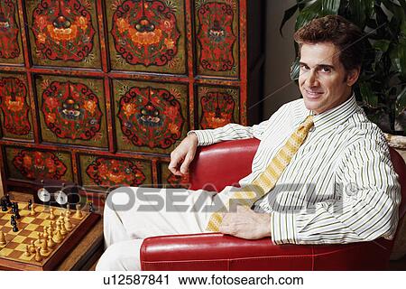 Portrait of a businessman sitting in an armchair and smiling View Large Photo Image Stock Image - Portrait of a businessman sitting in an armchair and smiling. Fotosearch