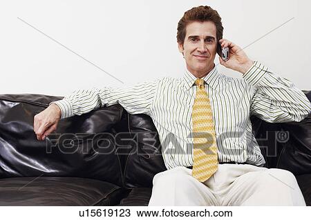 Stock Image - Portrait of a businessman sitting on a couch and talking on a mobile phone. Fotosearch