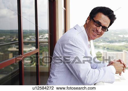 Stock Image - Portrait of a businessman standing in a balcony and smiling. Fotosearch