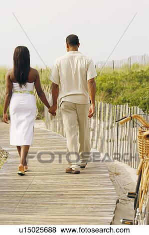 Stock Photo - Rear view of a couple walking on a boardwalk with holding their hands. Fotosearch
