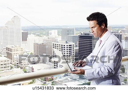 Stock Image - Side profile of a businessman using a laptop in a balcony. Fotosearch
