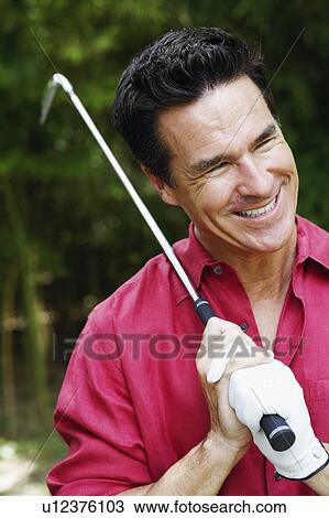 Stock Image - Close-up of a mature man holding a golf club and smiling. Fotosearch