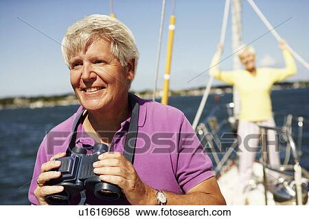 Close-up of a mature man holding a pair of binoculars in a boat with a mature woman standing behind him View Large Photo Image Stock Photo - Close-up of a mature man holding a pair of binoculars in a boat with a mature woman standing behind him. Fotosearch