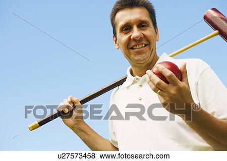 Stock Photo - Low angle view of a mature man holding a croquet mallet and a ball. Fotosearch