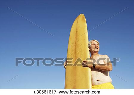 Low angle view of a mature man holding a surfboard View Large Photo Image Stock Photo - Low angle view of a mature man holding a surfboard. Fotosearch