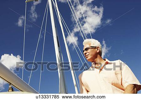 Stock Photography - Low angle view of a mature man standing in a sailboat. Fotosearch