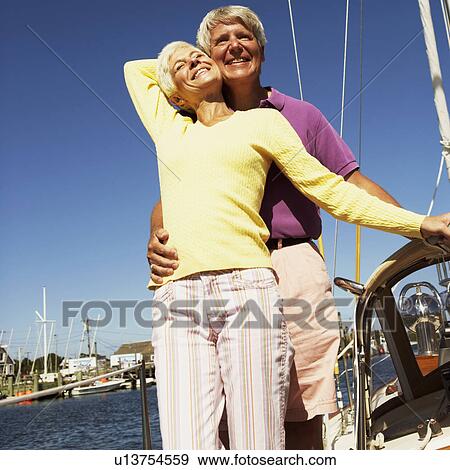Stock Photo - Low angle view of a mature man embracing a mature woman from behind in a boat and smiling. Fotosearch