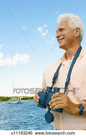 Mature man holding a pair of binoculars and smiling View Large Photo Image Stock Photograph - Mature man holding a pair of binoculars and smiling. Fotosearch