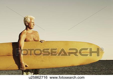 Mature man holding a surfboard under his arm View Large Photo Image Stock Photograph - Mature man holding a surfboard under his arm. Fotosearch