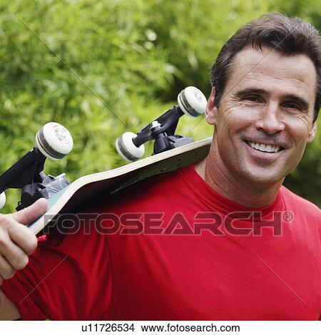 Portrait of a mature man carrying a skateboard on his shoulder and smiling View Large Photo Image Picture - Portrait of a mature man carrying a skateboard on his shoulder and smiling. Fotosearch
